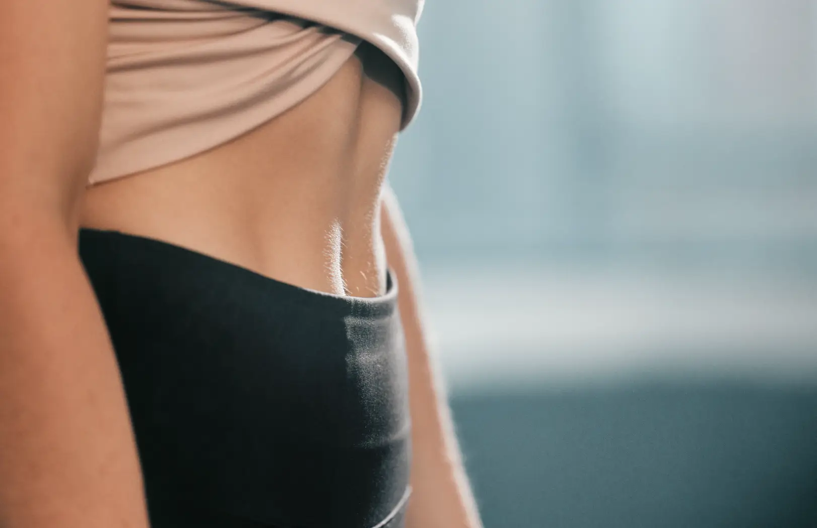 Close-up side view of a woman's waist and abdomen above black high-waisted clothing.