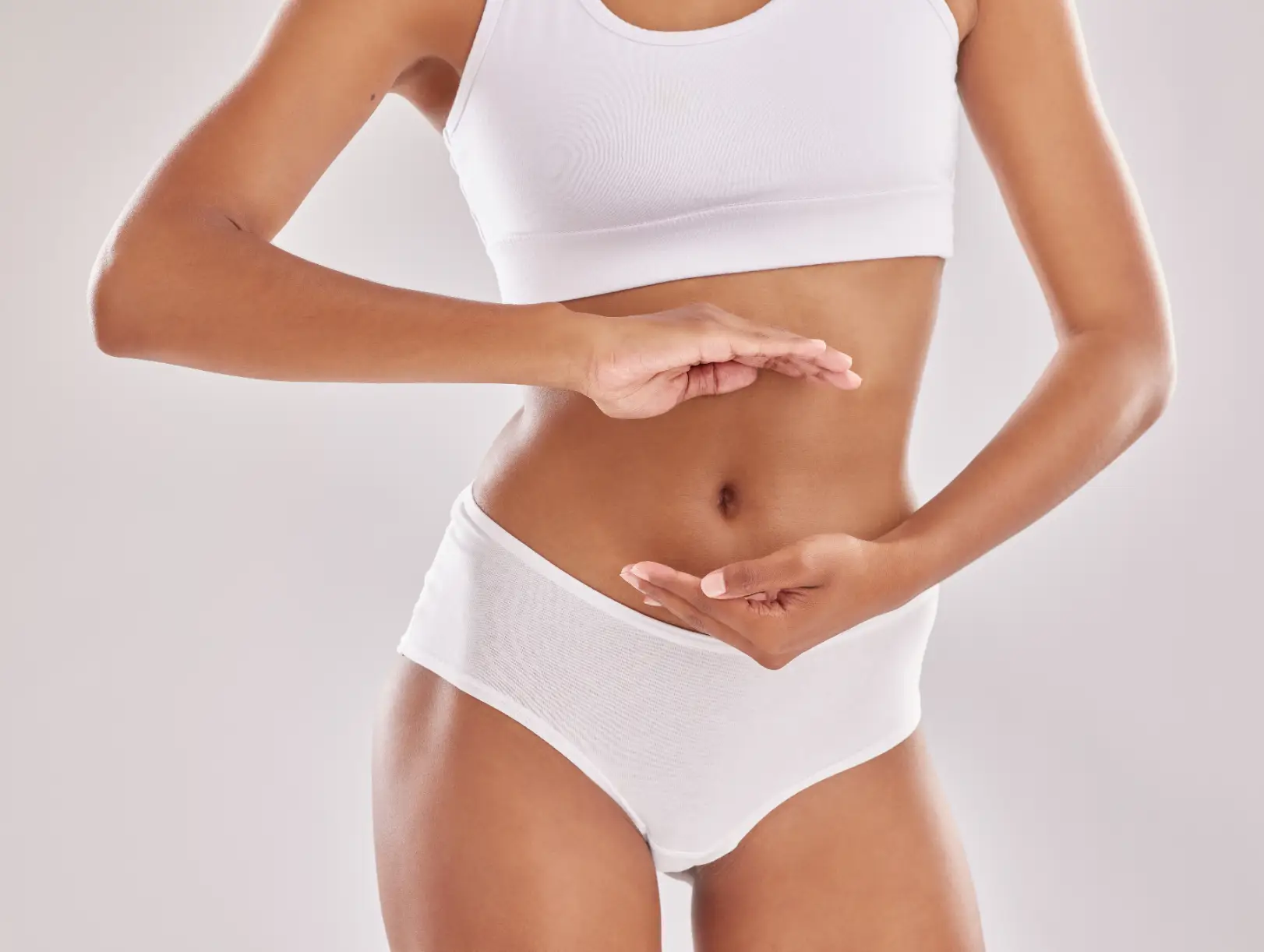 Woman in white athletic clothing holds both hands around the front of her abdomen.